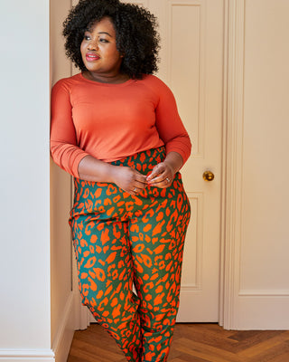 Woman wearing an orange long-sleeve top and green leggings with red leopard print on a white background. This top is the Stanway Raglan T-Shirt sewing pattern from "Ahead of the Curve" by Jenny Rushmore.