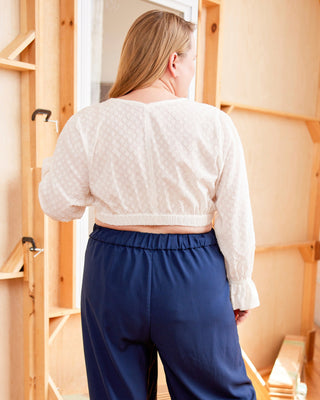 Person wearing a white top and blue pants standing in a room with wooden flooring and shelves. This top is the Kineton Dress & Top sewing pattern from Cashmerette.