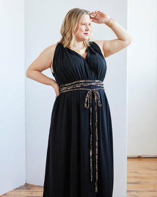 Woman wearing a black dress with a decorative belt in a room with wooden flooring. This dress is the Rockwell Dress sewing pattern from Cashmerette.