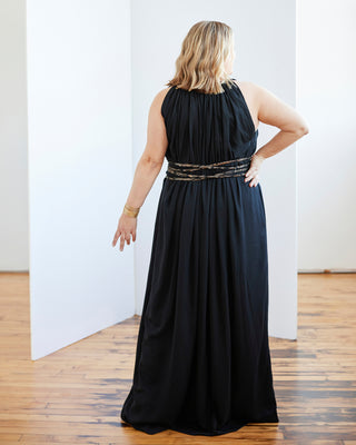 Woman wearing a black halter neck dress with gold accents in a minimal indoor setting. This dress is the Rockwell Dress sewing pattern from Cashmerette.