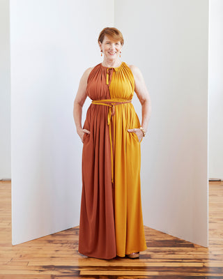Woman wearing a two-tone dress with rust and mustard colors standing in a minimalistic room. This dress is the Rockwell Dress sewing pattern from Cashmerette.