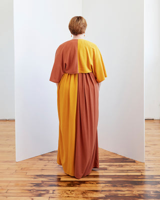Person wearing a two-tone dress with yellow and brown colors standing in a room with wooden flooring. The topper is the Caroll Shrug sewing pattern from Cashmerette.
