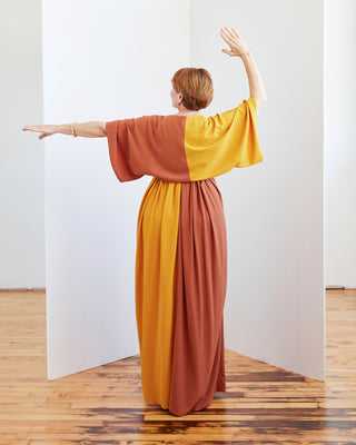 Woman wearing a two-tone dress with orange and yellow colors, standing in a minimalistic room. The topper is the Caroll Shrug sewing pattern from Cashmerette.