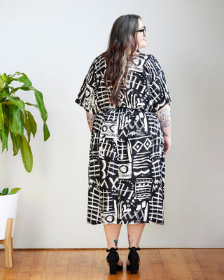Person wearing a black and white patterned dress standing in a room with a plant and wooden floor. This dress is the Franconia Dress sewing pattern from Cashmerette.