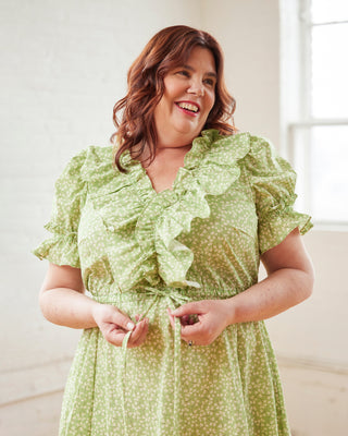 Woman wearing a green floral dress indoors with a neutral background. This dress is the Loring Dress sewing pattern from Cashmerette.