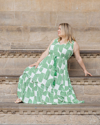 Woman in a green and white patterned dress sitting on stone steps. This dress is the Loring Dress sewing pattern from Cashmerette.