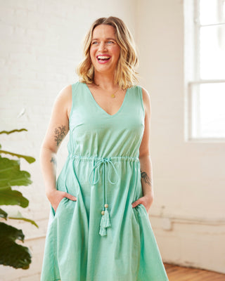 Woman wearing a light green dress indoors with a plant in the background. This dress is the Loring Dress sewing pattern from Cashmerette.