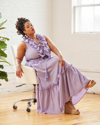 Woman in a lavender dress sitting on a chair in a bright room with a plant. This dress is the Loring Dress sewing pattern from Cashmerette.