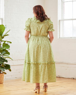Woman wearing a green floral dress standing in a room with a plant and white walls. This dress is the Loring Dress sewing pattern from Cashmerette.