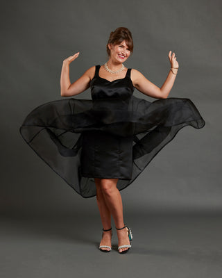 Woman wearing a black dress with a flowing skirt against a gray background. This dress is the Mansfield Dress sewing pattern from Cashmerette.
