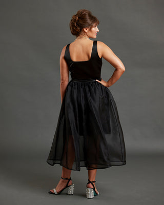 Woman wearing a black dress against a gray background. This dress is the Mansfield Dress sewing pattern from Cashmerette.
