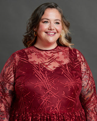 Woman wearing a red lace dress against a gray background. This dress is the Mansfield Dress sewing pattern from Cashmerette.