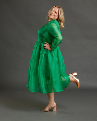 Woman wearing a green dress posing against a gray background. This dress is the Mansfield Dress sewing pattern from Cashmerette.
