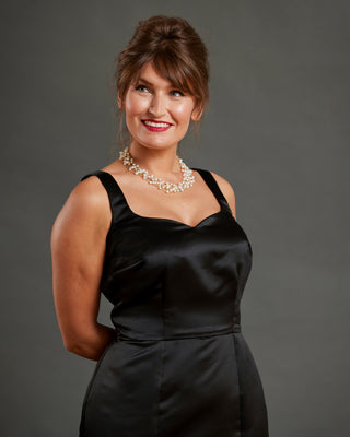 Woman wearing a black dress and pearl necklace against a gray background. This dress is the Mansfield Dress sewing pattern from Cashmerette.