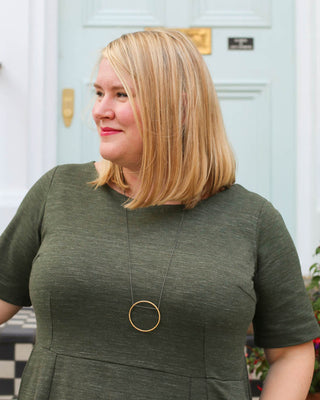 Woman wearing a green dress with a gold necklace in front of a light blue door. This dress is the Rivermont Dress & Top sewing pattern from Cashmerette.