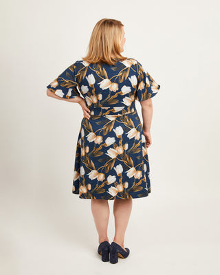 Woman wearing a floral dress with a plain background. This dress is the Alcott Dress sewing pattern from Cashmerette.