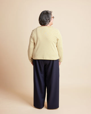 Person wearing a yellow striped shirt and navy pants on a beige background. This is the Grafton Dress, Top & Skirt sewing pattern from Cashmerette.