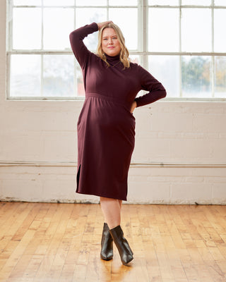 Woman wearing a burgundy dress standing in a room with large windows and wooden floor. This is the Grafton Dress, Top & Skirt sewing pattern from Cashmerette.
