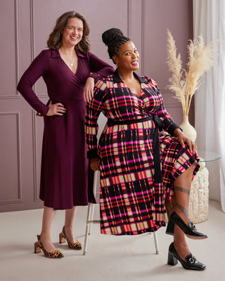 Two women posing together in front of a purple paneled wall. This is the Hazelton Wrap Dress sewing pattern from Cashmerette.