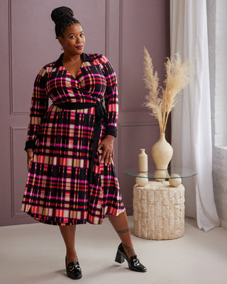 Woman wearing a plaid dress standing in a room with a decorative table and vase. This is the Hazelton Wrap Dress sewing pattern from Cashmerette.