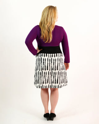 Person wearing a purple top and black and white patterned skirt on a white background. This dress is the Washington Dress sewing pattern from Cashmerette.