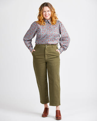 Woman wearing a floral blouse and green pants on a white background. This top is the Vernon Shirt sewing pattern from Cashmerette.