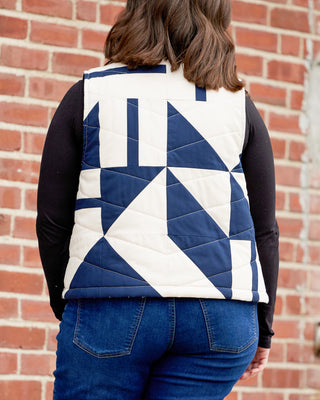 Person wearing a blue and white quilted vest against a brick wall. This vest is the Murcot Puffer Vest sewing pattern from Cashmerette.