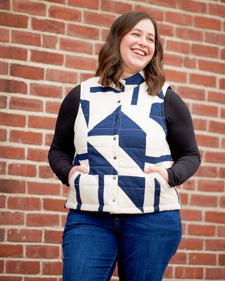 Woman wearing a blue and white quilted vest against a brick wall. This vest is the Murcot Puffer Vest sewing pattern from Cashmerette.