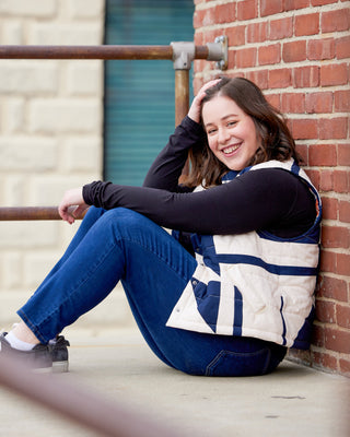 Person sitting against a brick wall wearing a blue and white jacket. This vest is the Murcot Puffer Vest sewing pattern from Cashmerette.