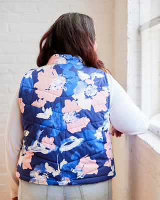 Person wearing a blue floral puffer vest in an indoor setting. This vest is the Murcot Puffer Vest sewing pattern from Cashmerette.