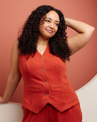 Woman wearing a red outfit against an orange background. This vest is the Hartwell Vest sewing pattern from Cashmerette.