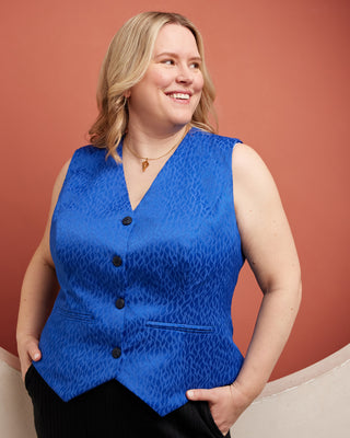 Woman wearing a blue vest against a red background. This vest is the Hartwell Vest sewing pattern from Cashmerette.