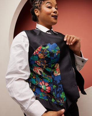 Person wearing a black vest with colorful floral embroidery against a red background. This vest is the Hartwell Vest sewing pattern from Cashmerette.