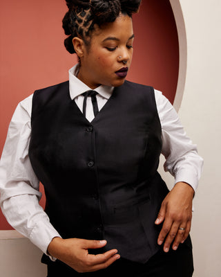 Person wearing a black vest over a white shirt with a red and beige background. This vest is the Hartwell Vest sewing pattern from Cashmerette.