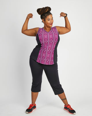 Woman flexing her muscles wearing a purple tank top and black capri pants on a white background. This top is the Spruce Workout Tank sewing pattern from Cashmerette.