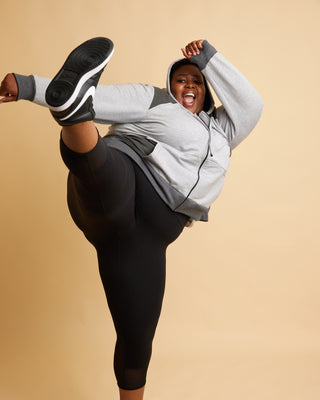 Person wearing a gray hoodie and black leggings on a beige background. This hoodie is the Stanton Hoodie sewing pattern from Cashmerette.