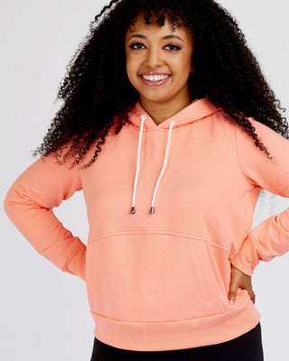 Person wearing a peach-colored hoodie on a plain background. This hoodie is the Stanton Hoodie sewing pattern from Cashmerette.