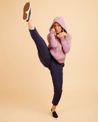 Person wearing a pink hoodie and navy pants on a beige background. This hoodie is the Stanton Hoodie sewing pattern from Cashmerette.
