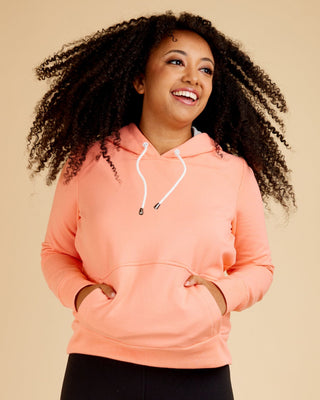 Woman wearing a pink hoodie and black leggings on a beige background. This hoodie is the Stanton Hoodie sewing pattern from Cashmerette.