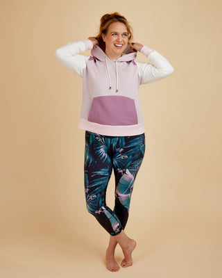 Woman wearing a light pink and purple hoodie with floral leggings on a beige background. This hoodie is the Stanton Hoodie sewing pattern from Cashmerette.