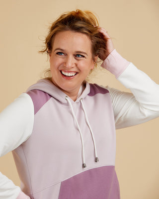 Woman wearing a light purple and white hoodie with a beige background. This hoodie is the Stanton Hoodie sewing pattern from Cashmerette.