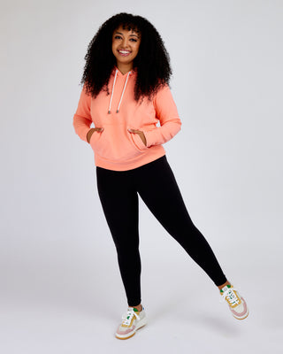 Woman wearing a peach hoodie and black leggings on a white background. This hoodie is the Stanton Hoodie sewing pattern from Cashmerette.