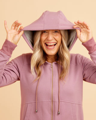 Person wearing a purple hoodie with a beige background. This hoodie is the Stanton Hoodie sewing pattern from Cashmerette.