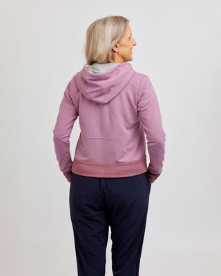 Person wearing a pink hoodie and dark pants on a light gray background. This hoodie is the Stanton Hoodie sewing pattern from Cashmerette.