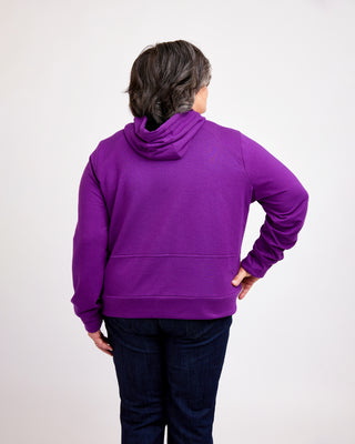 Person wearing a purple hoodie from behind on a white background. This hoodie is the Stanton Hoodie sewing pattern from Cashmerette.