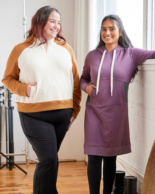 Two women wearing hoodies and black pants standing indoors.