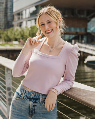 Woman in a pink top and blue jeans leaning on a railing by a waterfront. This top is the Carlyle square neck t-shirt sewing pattern from Cashmerette.