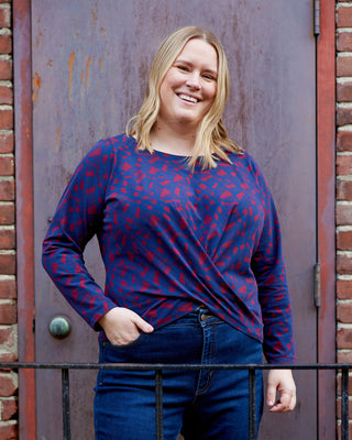 Woman wearing a blue and red patterned top standing in front of a rusty metal door. This top is the Brattle Twist Top sewing pattern from Cashmerette.