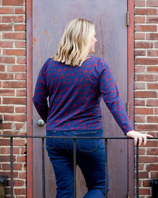Woman wearing a blue patterned sweater and jeans standing against a brick wall. This top is the Brattle Twist Top sewing pattern from Cashmerette.