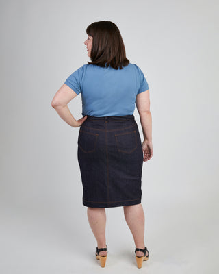 Woman wearing a blue t-shirt and dark denim skirt on a plain background. This skirt is the Ellis Denim Skirt sewing pattern from Cashmerette.